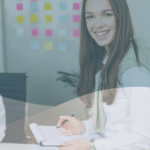 Two women in an office, one is smiling at the camera and the other is looking at something in her hands