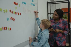 Teacher watching student draw letters on a whiteboard