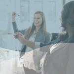 Two women smiling and drawing on a school whiteboard