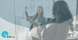 Two women smiling and drawing on a school whiteboard